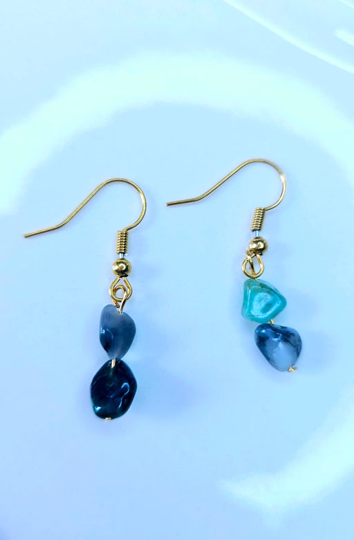 A pair of handcrafted emerald birthstone earrings with dangling natural stones, displayed against a neutral background