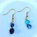 A pair of handcrafted emerald birthstone earrings with dangling natural stones, displayed against a neutral background