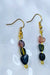 An image displaying a pair of handmade tourmaline three-stone dangle hook earrings, showcasing black, green, and pink tourmaline beads, against a soft background